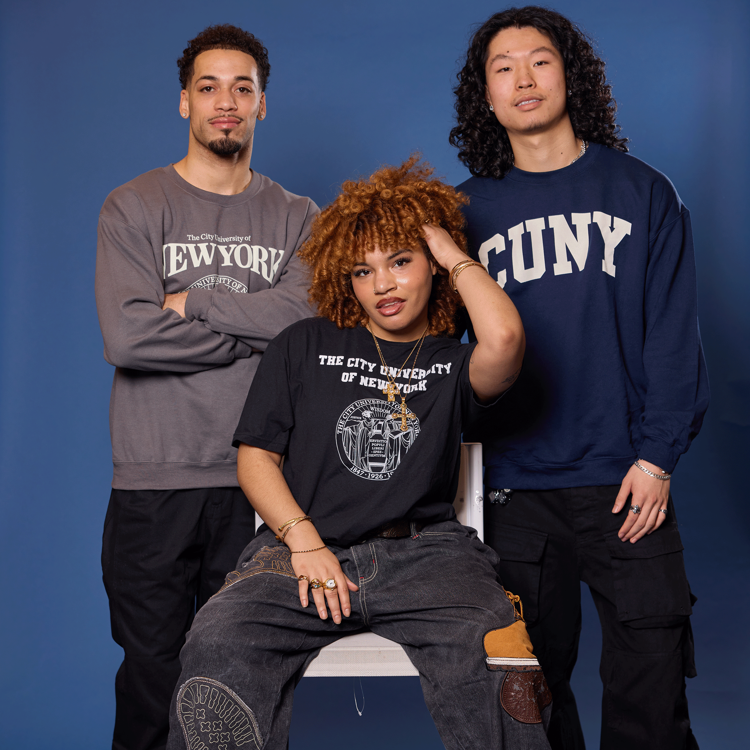 Three people wearing NYU and SUNY sweatshirts against a blue background